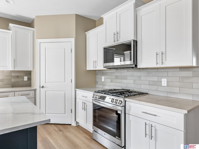 kitchen with stainless steel appliances, light hardwood / wood-style floors, white cabinets, backsplash, and light stone countertops