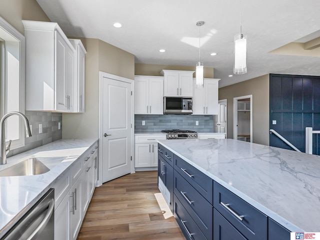 kitchen with blue cabinets, light hardwood / wood-style flooring, hanging light fixtures, white cabinetry, and appliances with stainless steel finishes