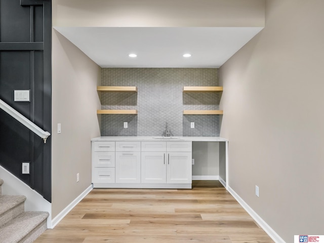 kitchen with tasteful backsplash, white cabinetry, sink, and light hardwood / wood-style floors