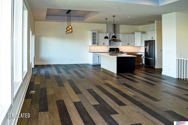 kitchen featuring a center island with sink, pendant lighting, white cabinets, stainless steel fridge, and dark wood-type flooring