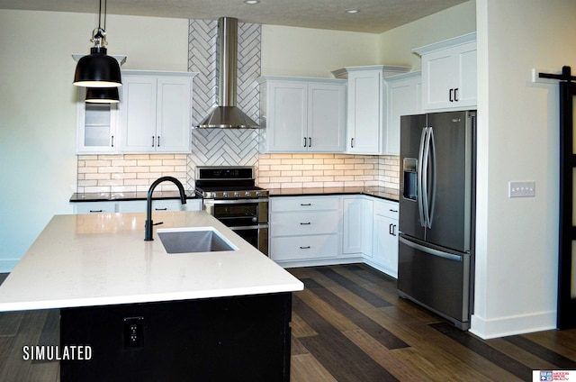 kitchen featuring stainless steel appliances, a center island with sink, sink, a barn door, and wall chimney range hood