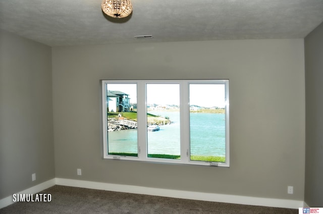 unfurnished room with a textured ceiling, a water view, and carpet floors