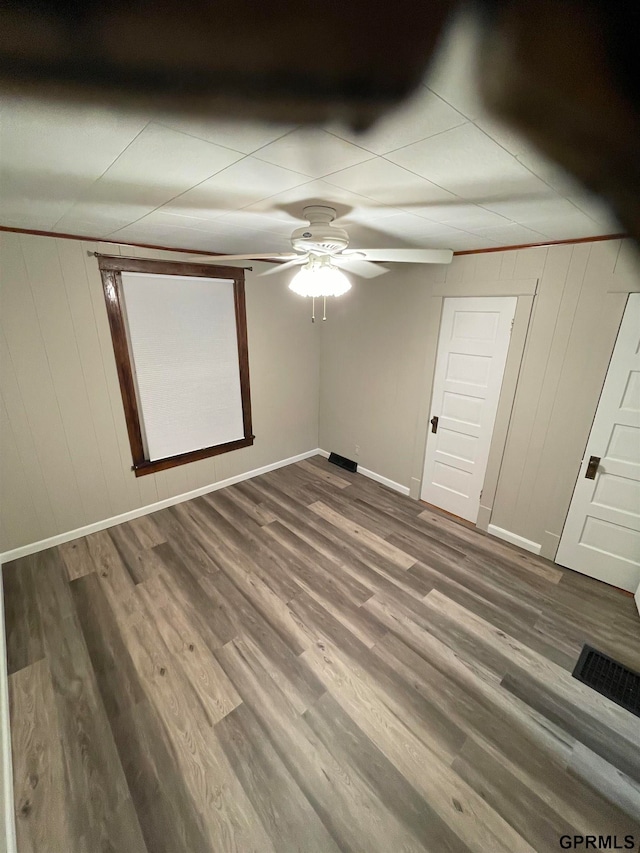 unfurnished bedroom featuring dark hardwood / wood-style floors, ceiling fan, and wood walls