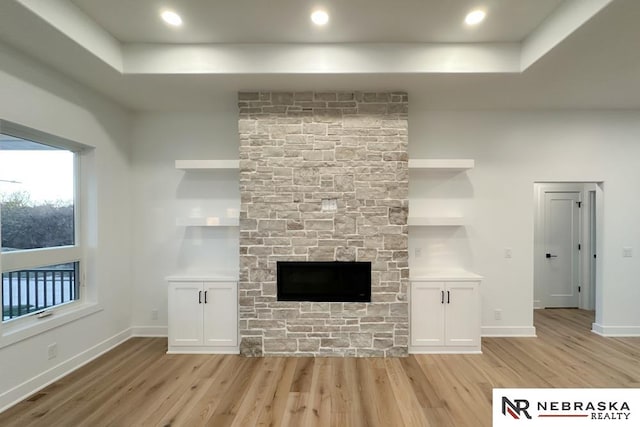 unfurnished living room featuring a fireplace, a tray ceiling, and light hardwood / wood-style floors