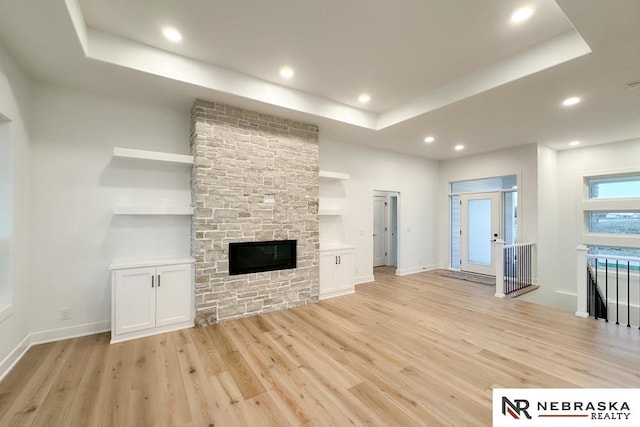 unfurnished living room with a raised ceiling, light hardwood / wood-style floors, and a stone fireplace