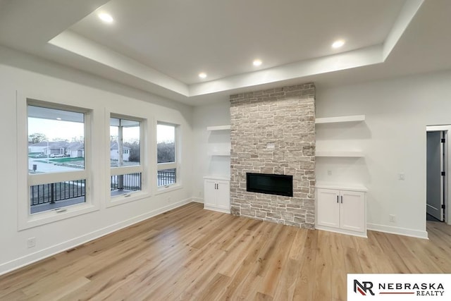 unfurnished living room with a raised ceiling, light wood-type flooring, and a stone fireplace