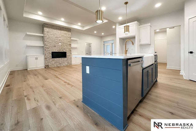 kitchen with stainless steel dishwasher, pendant lighting, light hardwood / wood-style floors, a center island with sink, and white cabinets