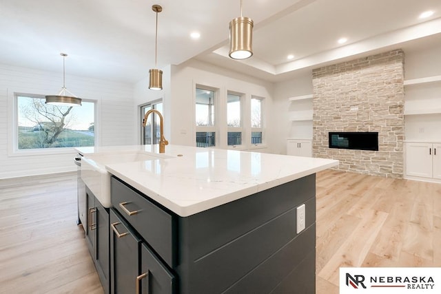 kitchen featuring a stone fireplace, light hardwood / wood-style flooring, an island with sink, and pendant lighting