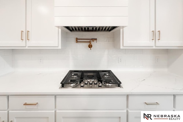 room details featuring premium range hood, stainless steel gas stovetop, white cabinetry, and light stone counters