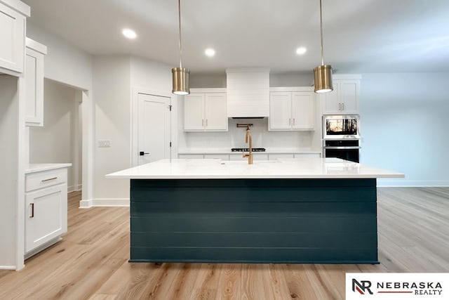 kitchen with decorative light fixtures, white cabinetry, a center island with sink, and light hardwood / wood-style floors