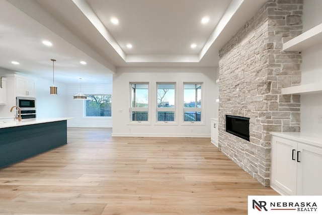 unfurnished living room featuring a raised ceiling, light wood-type flooring, and a stone fireplace