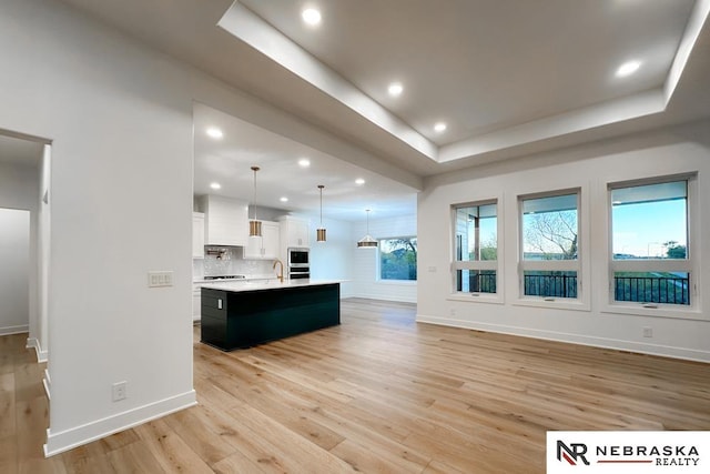 kitchen featuring white cabinets, a tray ceiling, pendant lighting, a kitchen island with sink, and light hardwood / wood-style floors