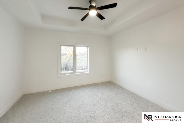 empty room featuring ceiling fan, a raised ceiling, and carpet floors