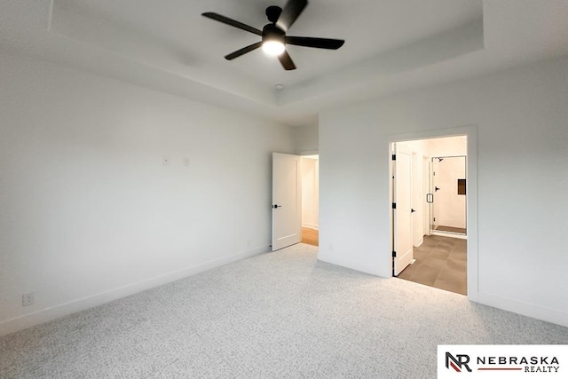 unfurnished bedroom featuring a tray ceiling, ceiling fan, and ensuite bathroom