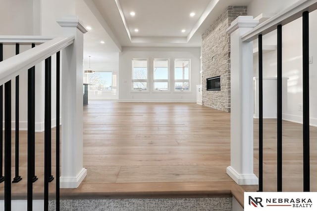 unfurnished living room featuring hardwood / wood-style floors, a stone fireplace, and a raised ceiling