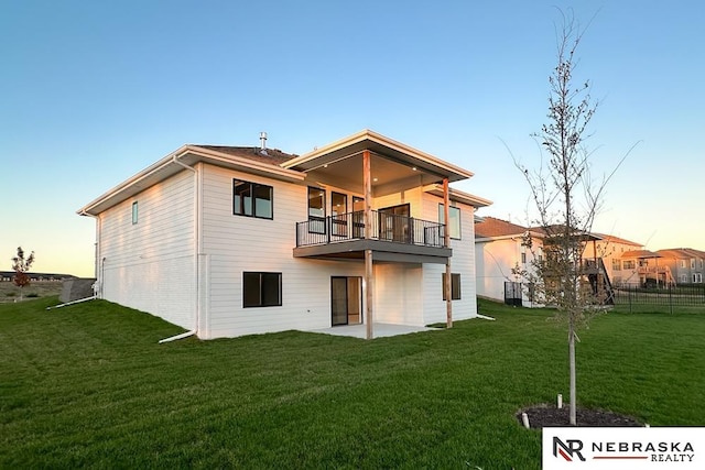 back house at dusk featuring a lawn, a patio, and a balcony