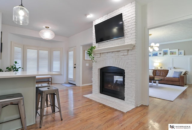 living room with light hardwood / wood-style flooring, an inviting chandelier, ornamental molding, and a brick fireplace