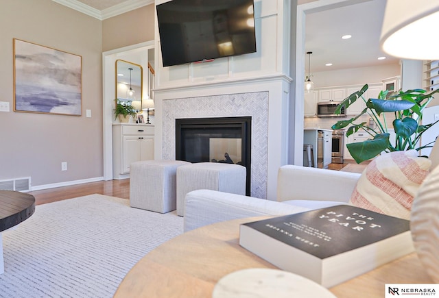 living room featuring light hardwood / wood-style floors, ornamental molding, and a tiled fireplace