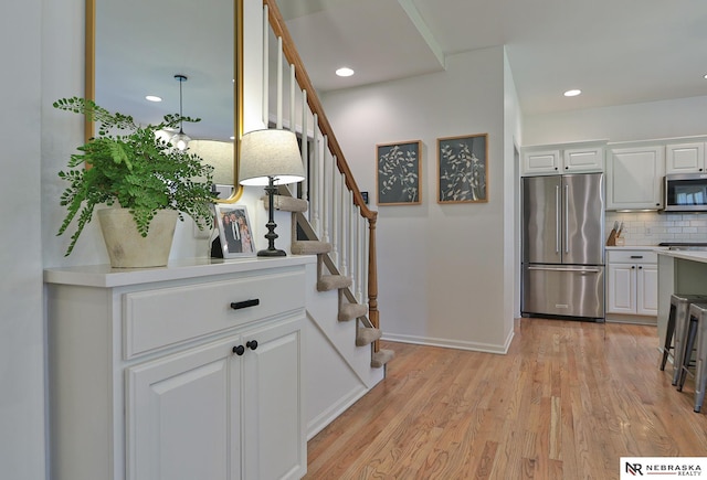 interior space featuring decorative backsplash, light hardwood / wood-style flooring, white cabinets, and appliances with stainless steel finishes