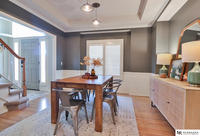 dining room featuring a raised ceiling, crown molding, and light hardwood / wood-style flooring