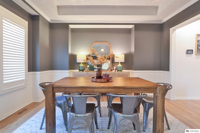 dining area featuring ornamental molding, a tray ceiling, and light wood-type flooring