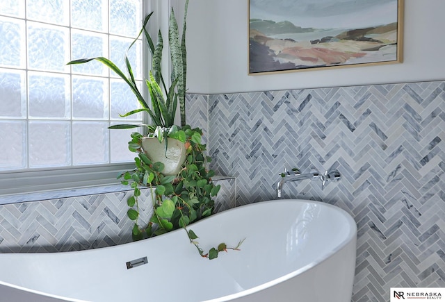 bathroom with a tub to relax in, plenty of natural light, and tile walls