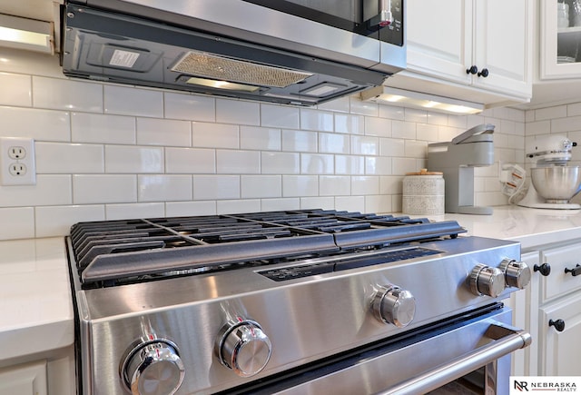 interior details with appliances with stainless steel finishes, backsplash, and white cabinetry