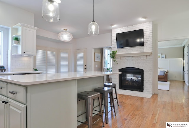 kitchen with a brick fireplace, light hardwood / wood-style floors, decorative light fixtures, a breakfast bar, and white cabinets