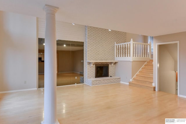 unfurnished living room with hardwood / wood-style flooring, a brick fireplace, and ornate columns