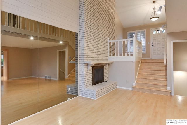 unfurnished living room with a brick fireplace, a towering ceiling, and hardwood / wood-style floors