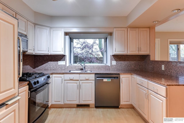 kitchen featuring sink, tasteful backsplash, light hardwood / wood-style flooring, dark stone counters, and black appliances