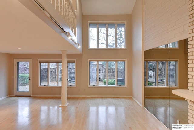 unfurnished living room with a towering ceiling, light hardwood / wood-style flooring, and ornate columns