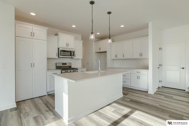 kitchen with a kitchen island with sink, white cabinets, sink, light hardwood / wood-style floors, and stainless steel appliances