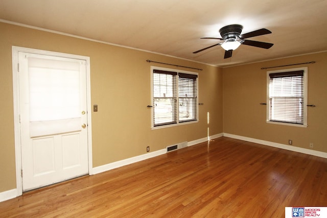 empty room with wood-type flooring, a wealth of natural light, ornamental molding, and ceiling fan