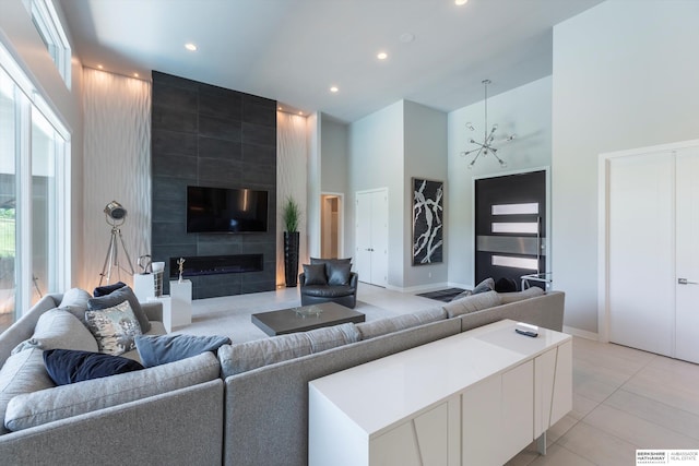 living room featuring a fireplace, light tile patterned floors, a towering ceiling, and a chandelier