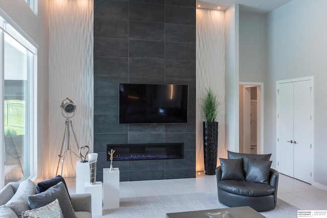 living room with a tile fireplace, a towering ceiling, tile patterned flooring, and a healthy amount of sunlight