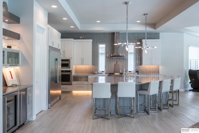 kitchen featuring wine cooler, white cabinetry, built in refrigerator, and wall chimney range hood