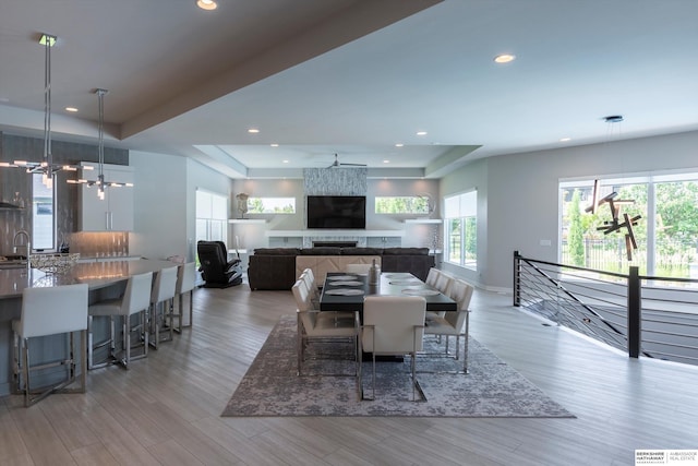 dining room featuring ceiling fan with notable chandelier, light wood-type flooring, and a large fireplace