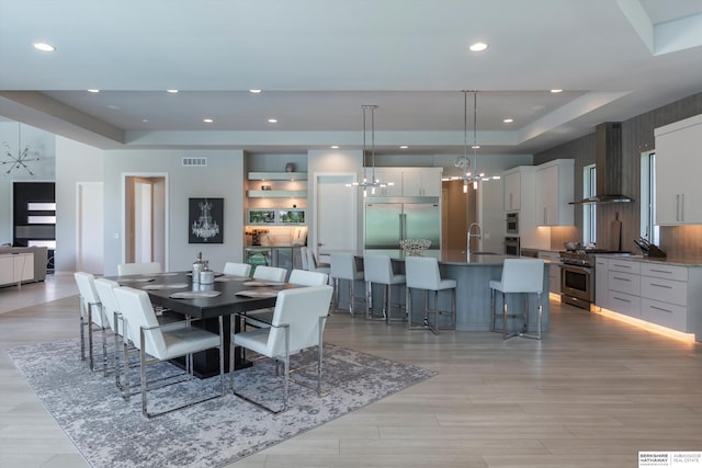 dining area featuring a notable chandelier, a raised ceiling, light wood-type flooring, and sink