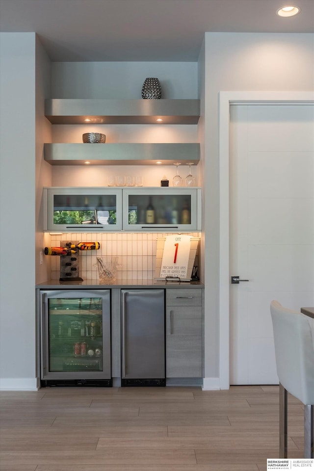 bar featuring stainless steel fridge, light hardwood / wood-style flooring, wine cooler, and tasteful backsplash