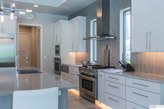 kitchen featuring white cabinetry, sink, hanging light fixtures, wall chimney range hood, and appliances with stainless steel finishes