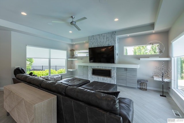 living room with ceiling fan, light wood-type flooring, a fireplace, and a wealth of natural light