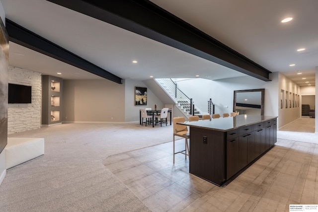 kitchen featuring a center island, light colored carpet, dark brown cabinetry, and beam ceiling