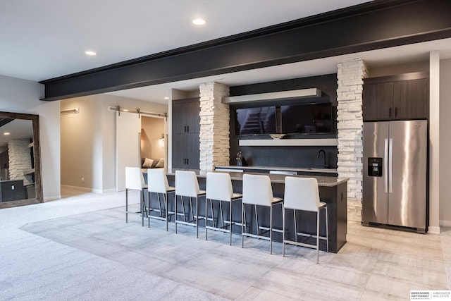 kitchen with stainless steel fridge, a breakfast bar, dark brown cabinets, a barn door, and a kitchen island