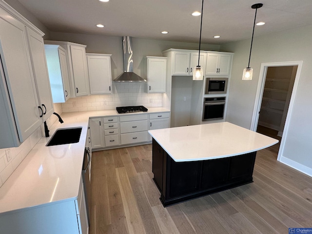 kitchen with sink, wall chimney exhaust hood, appliances with stainless steel finishes, a kitchen island, and white cabinetry