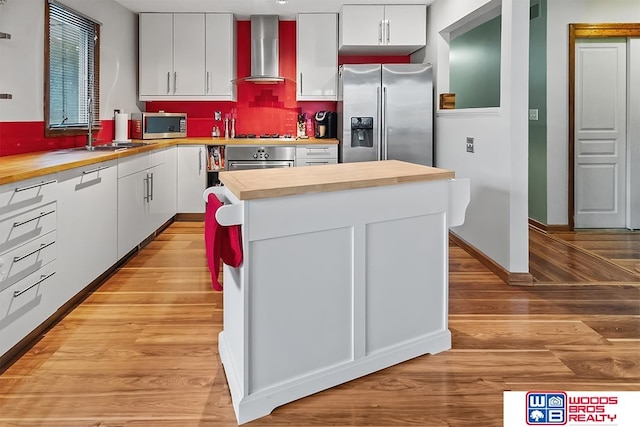 kitchen featuring stainless steel appliances, white cabinetry, and wall chimney exhaust hood