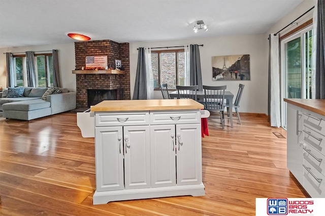 kitchen with a fireplace, white cabinets, light hardwood / wood-style floors, and wood counters