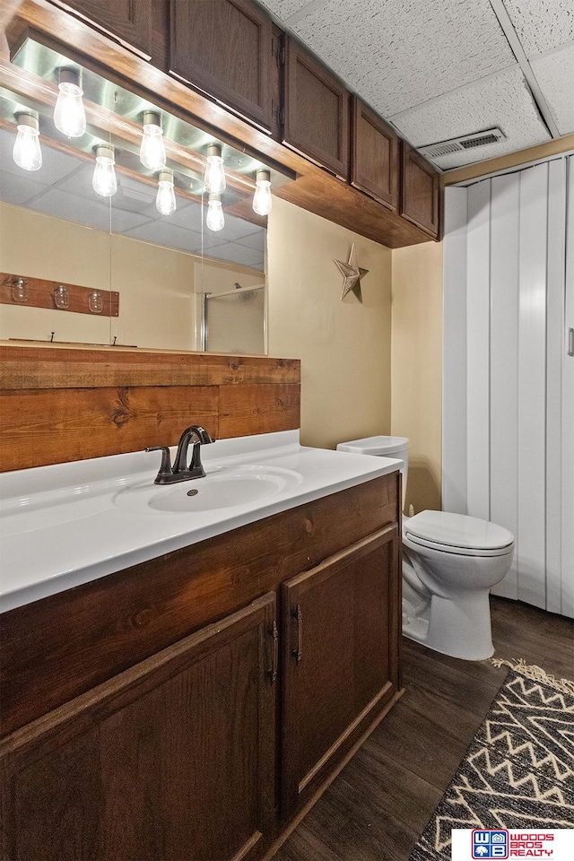 bathroom with a paneled ceiling, vanity, wood-type flooring, and toilet