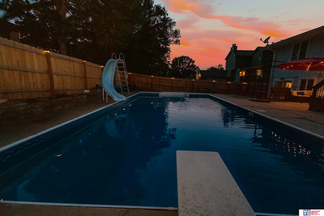 pool at dusk with a diving board and a water slide