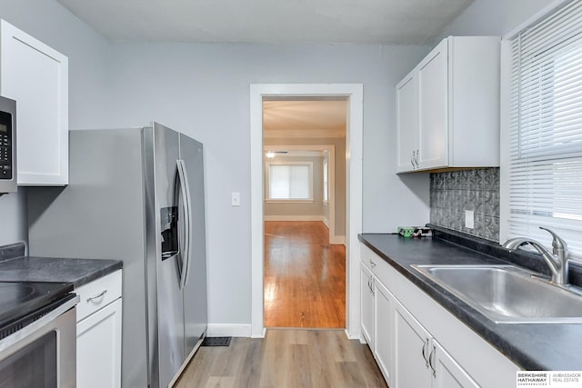 kitchen featuring decorative backsplash, light wood-type flooring, stainless steel range with electric stovetop, sink, and white cabinetry